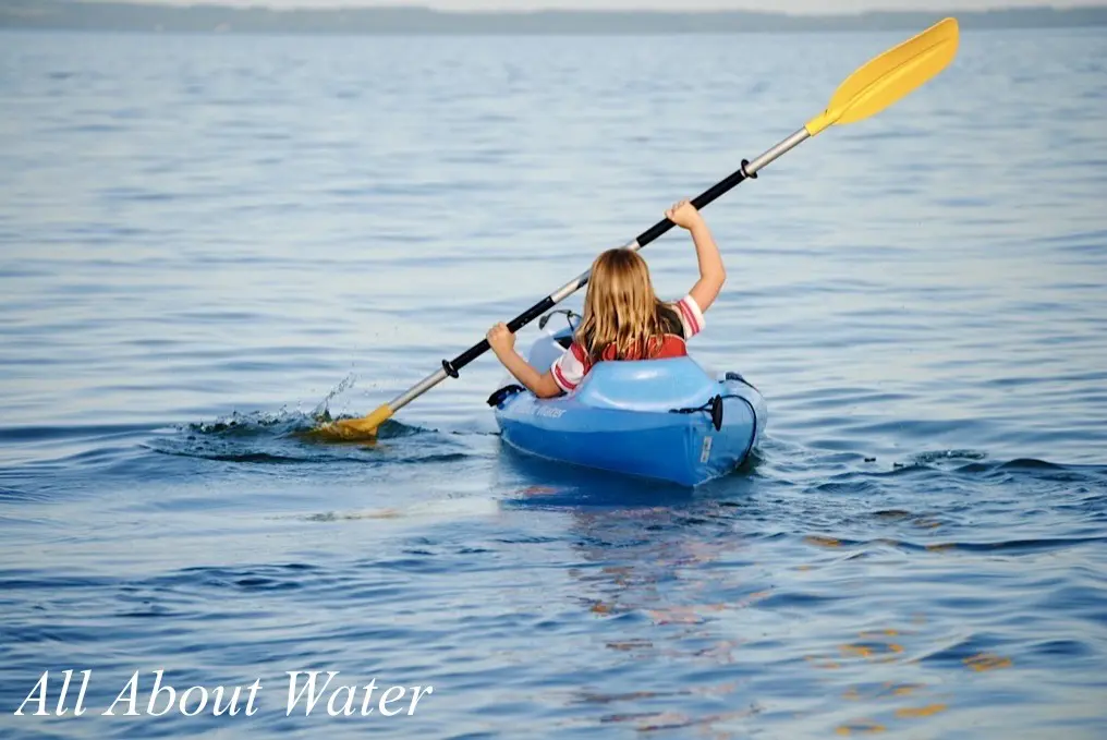A young girl kayaking on a calm lake.