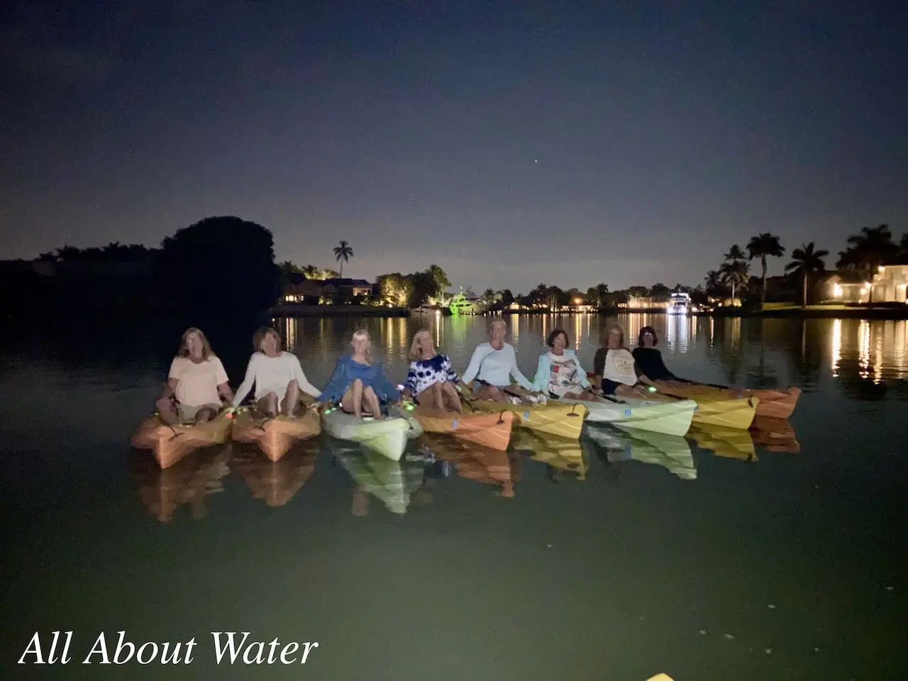 Six people kayaking at night in a canal.
